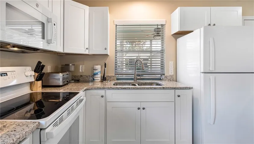 Kitchen with white appliances, a toaster, white cabinets, light stone counters, and a sink