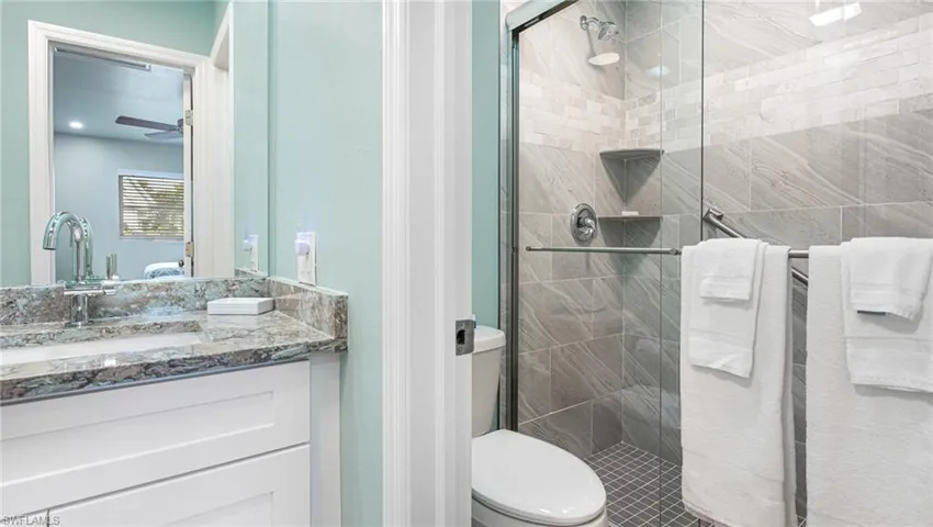 Full bathroom with a ceiling fan, a stall shower, vanity, and toilet