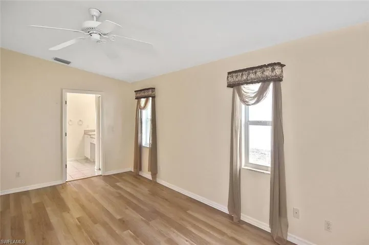 Unfurnished bedroom with light wood finished floors, ensuite bath, a ceiling fan, and lofted ceiling