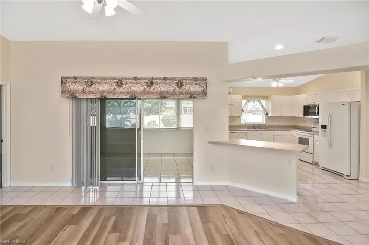 Kitchen with ceiling fan, white appliances, light tile patterned floors, white cabinets, and a peninsula