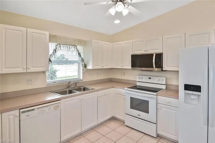 Kitchen with white appliances, light tile patterned floors, light countertops, white cabinetry, and lofted ceiling