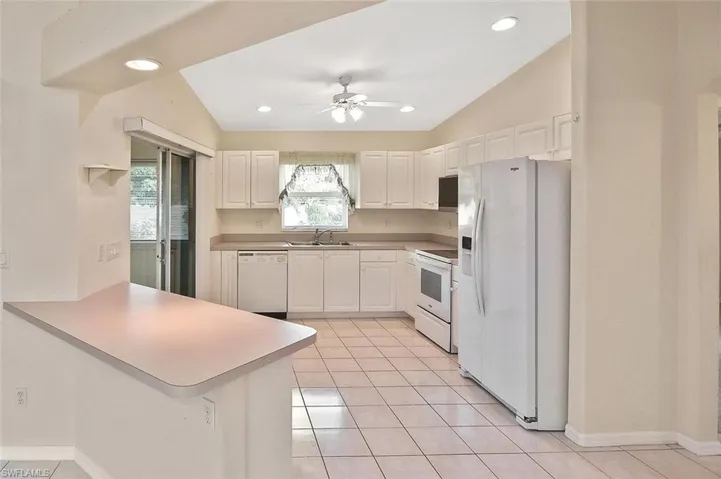 Kitchen featuring white appliances, light tile patterned floors, white cabinetry, recessed lighting, and a peninsula