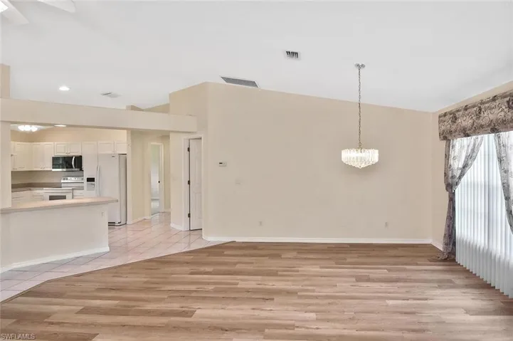 Kitchen with white appliances, hanging light fixtures, a chandelier, white cabinets, and a peninsula