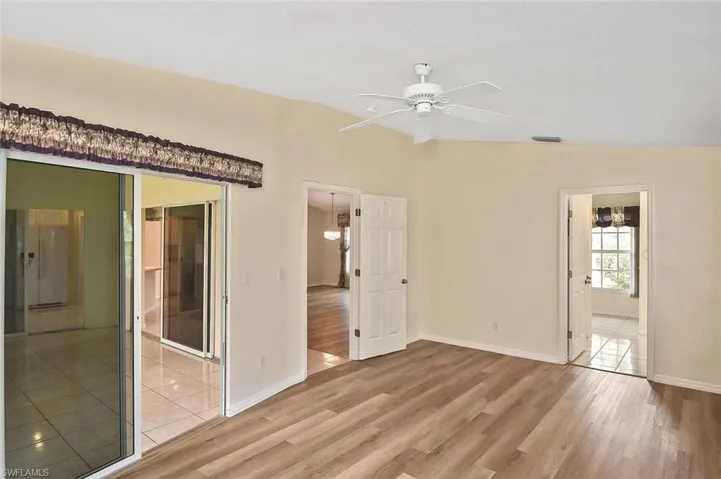 Unfurnished bedroom featuring light wood-style floors, lofted ceiling, freestanding refrigerator, ceiling fan, and ensuite bath