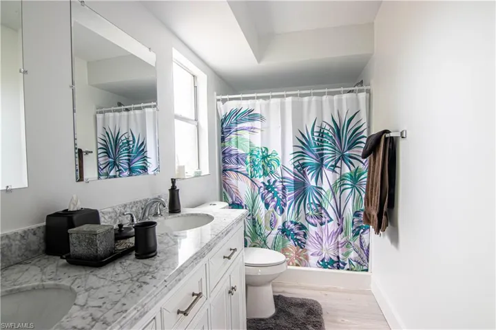Bathroom featuring double vanity, a shower with shower curtain, and light wood-type flooring