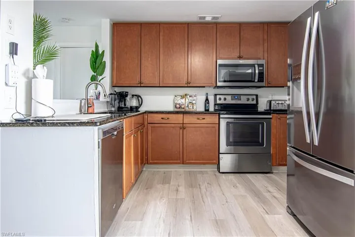 Kitchen with stainless steel appliances, wood finish cabinets, dark stone countertops, a peninsula, and light wood-style flooring
