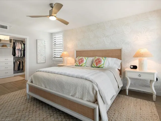 Bedroom with wood finished floors, a ceiling fan, a walk in closet, and wallpapered walls