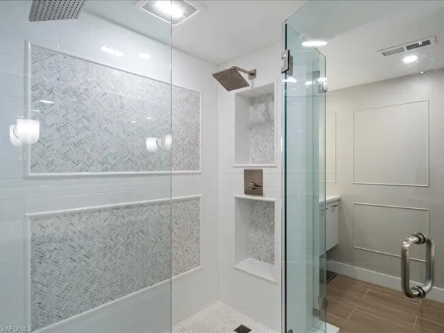 Bathroom featuring tiled shower, vanity, and wood finish floors