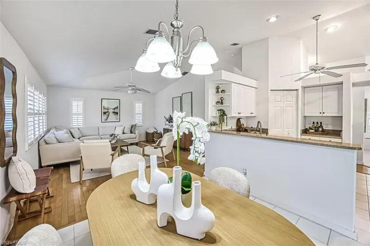 Dining area featuring ceiling fan with notable chandelier, vaulted ceiling, and light hardwood / wood-style flooring