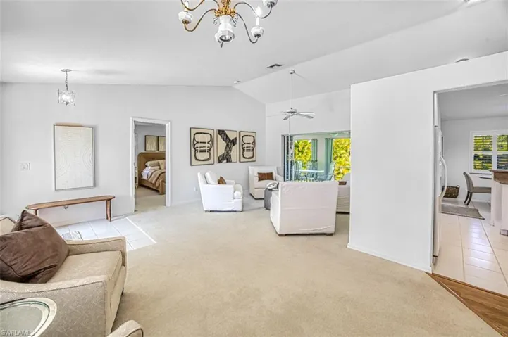Living room with lofted ceiling, ceiling fan with notable chandelier, and carpet floors