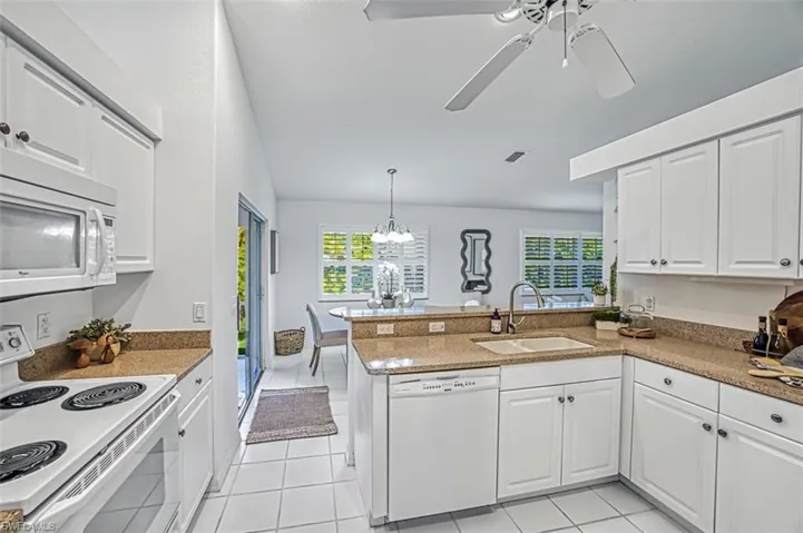 Kitchen with white appliances, kitchen peninsula, white cabinets, ceiling fan with notable chandelier, and sink