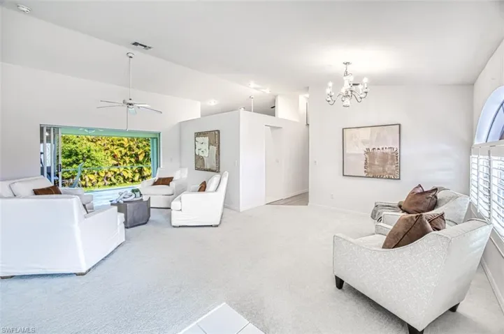 Carpeted living room featuring ceiling fan with notable chandelier and vaulted ceiling