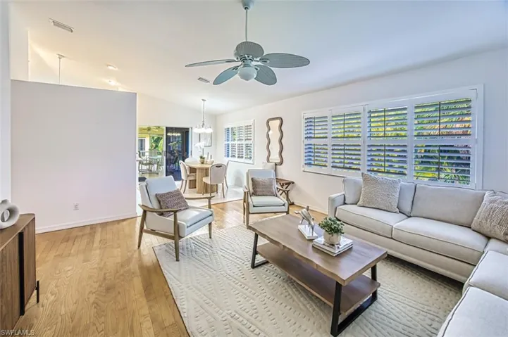 Living room with wood-type flooring, ceiling fan with notable chandelier, and vaulted ceiling