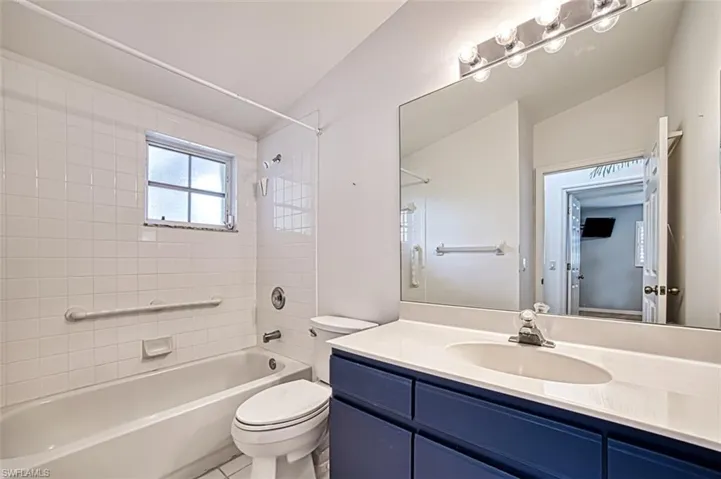 Full bathroom featuring vanity, vaulted ceiling, tiled shower / bath combo, toilet, and tile patterned flooring