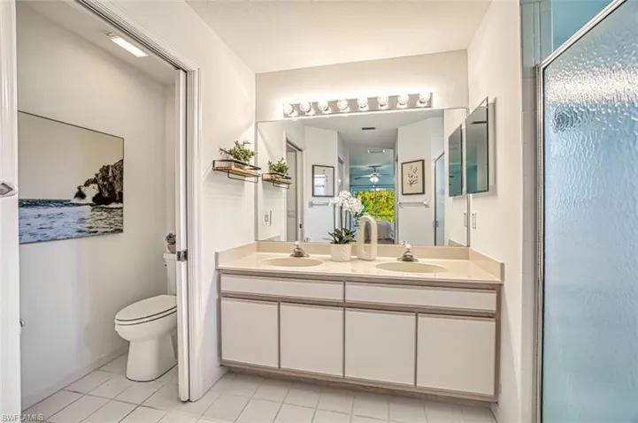 Bathroom with a shower with door, tile patterned flooring, toilet, and dual bowl vanity