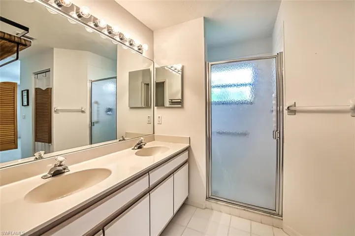 Bathroom with tile patterned floors, a shower with shower door, and dual bowl vanity