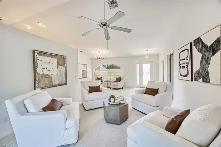 Living room featuring ceiling fan with notable chandelier, vaulted ceiling, and carpet floors