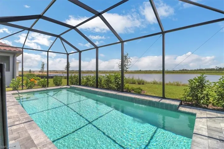 Swimming pool with a sunroom, glass enclosure, a water view, and a lawn