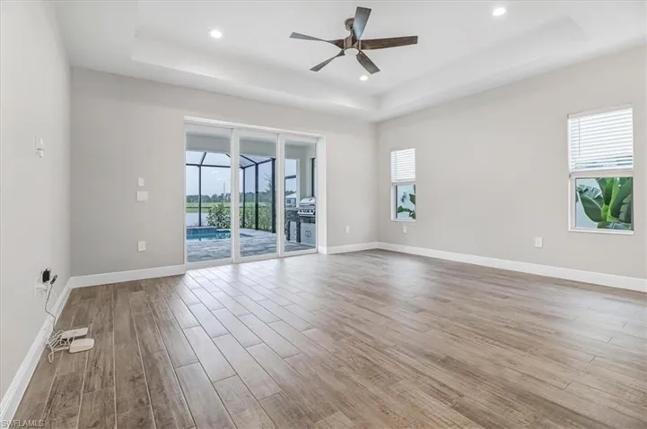 Unfurnished room featuring ceiling fan, a raised ceiling, healthy amount of natural light, light wood finished floors, and a sunroom