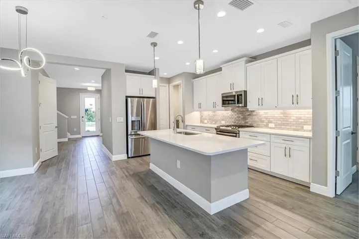 Kitchen featuring stainless steel appliances, white cabinetry, a center island with sink, backsplash, and light wood-style floors