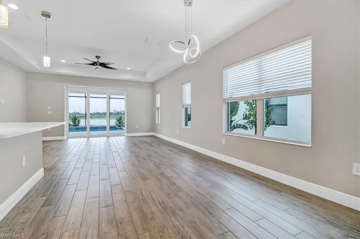 Unfurnished living room featuring a raised ceiling, light wood-style flooring, a ceiling fan, and recessed lighting