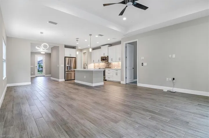 Kitchen featuring open floor plan, white cabinetry, ceiling fan, a kitchen island with sink, and stainless steel appliances