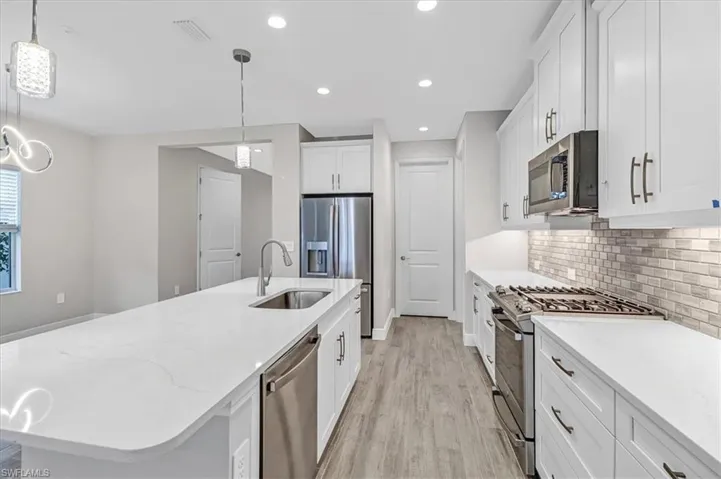 Kitchen featuring stainless steel appliances, a center island with sink, light stone countertops, white cabinets, and light wood-style flooring