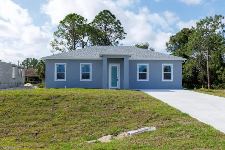Ranch-style house featuring concrete driveway, a front lawn, a shingled roof, and stucco siding