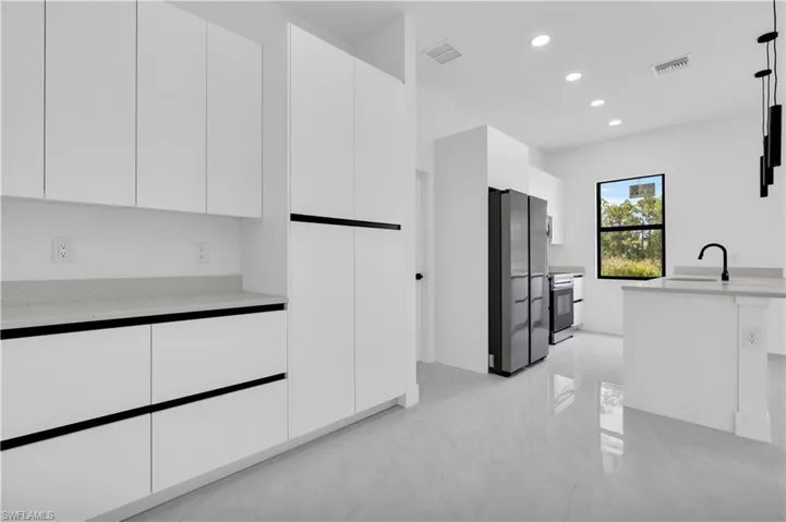 Kitchen with freestanding refrigerator, modern cabinets, light marble finish floors, white cabinetry, and recessed lighting