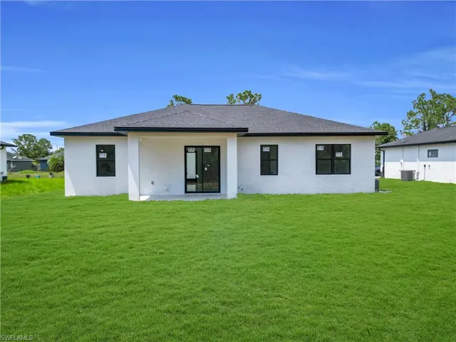 Rear view of house featuring a yard, stucco siding, and a shingled roof