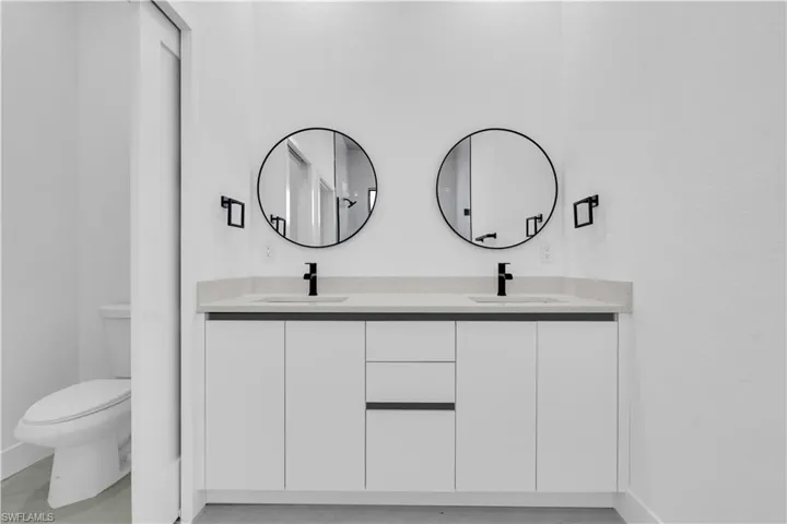 Full bathroom featuring toilet, double vanity, and baseboards