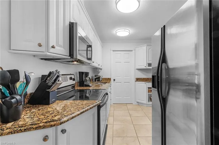 Kitchen with white cabinets, light tile patterned flooring, ornamental molding, stainless steel appliances, and dark stone counters