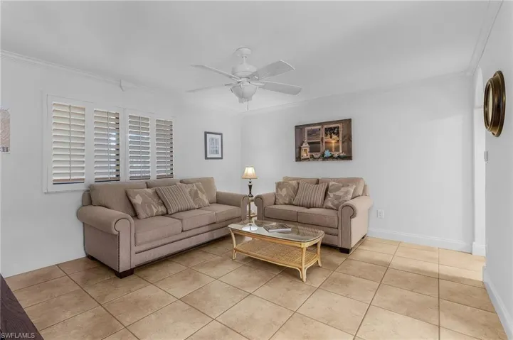 Living room with ceiling fan, light tile patterned floors, and ornamental molding