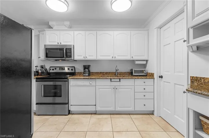 Kitchen featuring appliances with stainless steel finishes, white cabinets, light tile patterned floors, dark stone counters, and ornamental molding