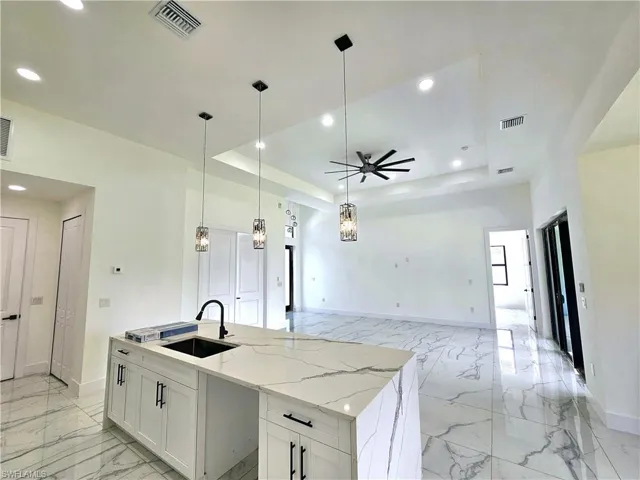 Kitchen featuring white cabinets, a raised ceiling, an island with sink, and ceiling fan