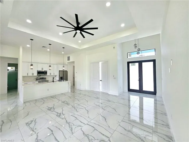 Unfurnished living room featuring a raised ceiling, french doors, sink, ceiling fan, and light tile patterned flooring