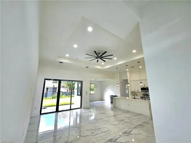 Unfurnished living room with ceiling fan, sink, a tray ceiling, and light tile patterned flooring