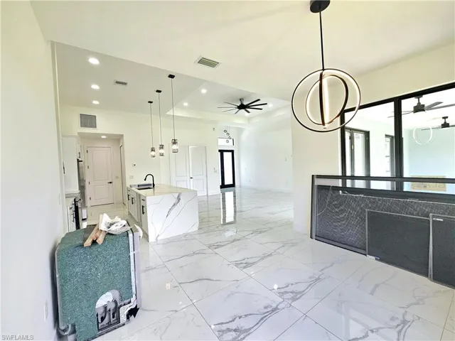 Kitchen with ceiling fan with notable chandelier, light tile patterned floors, hanging light fixtures, a raised ceiling, and a center island with sink
