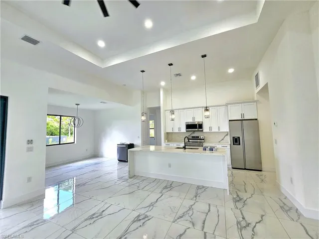 Kitchen with a kitchen island with sink, white cabinetry, light tile patterned floors, stainless steel appliances, and sink