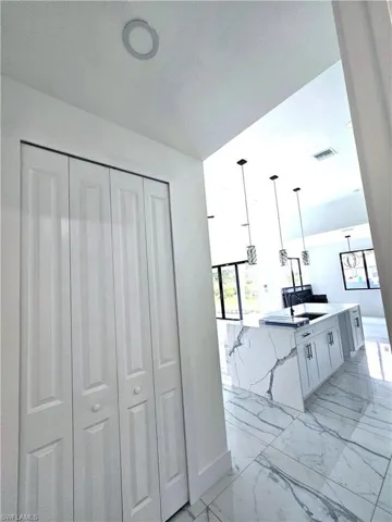 Kitchen with white cabinets, light tile patterned floors, decorative light fixtures, light stone countertops, and sink