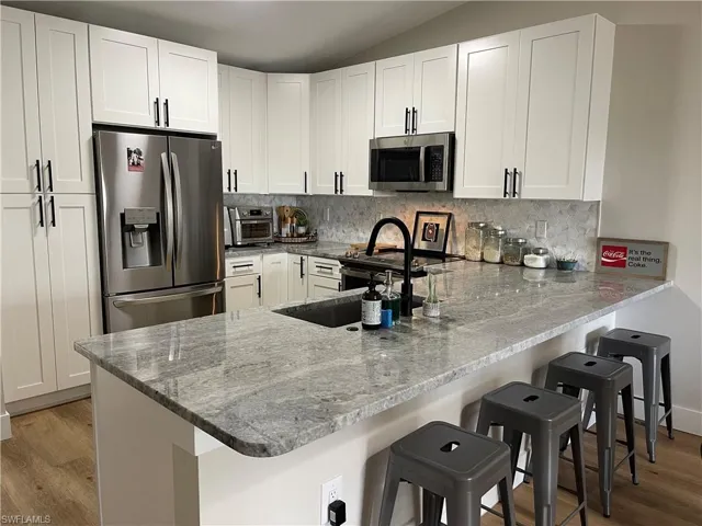 Kitchen with appliances with stainless steel finishes, white cabinetry, a breakfast bar area, and kitchen peninsula