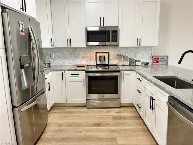 Kitchen featuring stainless steel appliances, backsplash, white cabinetry, light stone countertops, and light wood-type flooring