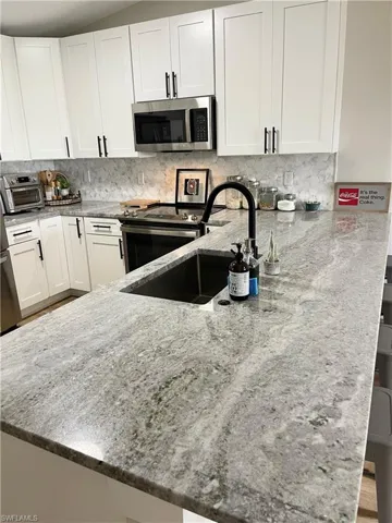 Kitchen with light stone countertops, stainless steel appliances, white cabinets, kitchen peninsula, and backsplash