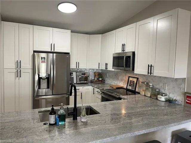 Kitchen featuring stainless steel appliances, kitchen peninsula, white cabinets, and tasteful backsplash