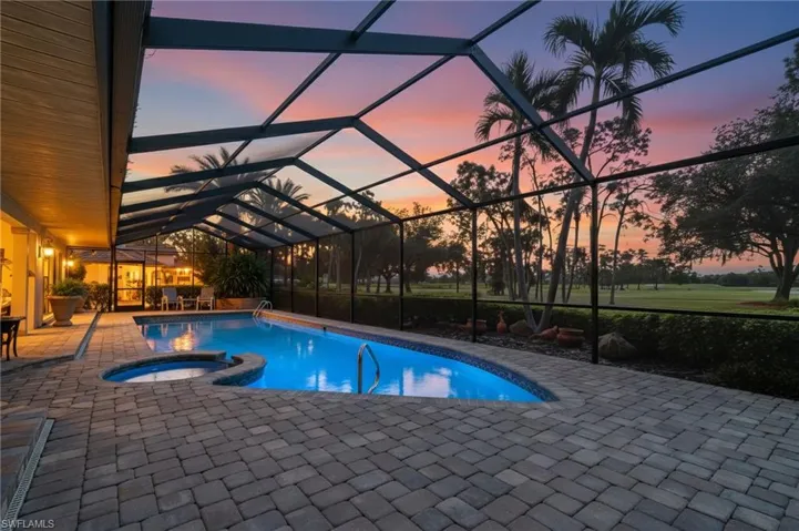 Pool at dusk featuring a sunroom, a lanai, a patio area, and a pool with connected hot tub