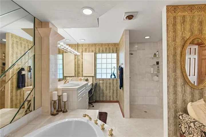 Bathroom with a bath, walk in shower, vanity, and light tiled floors.
