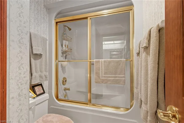 Bathroom with bath / shower combo with glass door and toilet