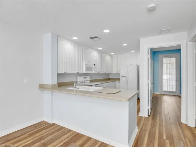 Kitchen with light hardwood / wood-style flooring, kitchen peninsula, and white appliances