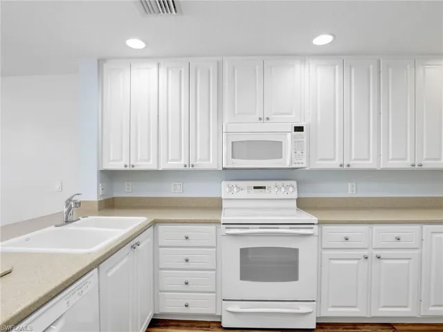 Kitchen with dark wood-type flooring, white appliances, white cabinetry, and sink
