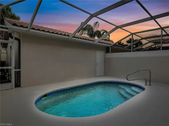 Pool at dusk featuring a patio area and glass enclosure